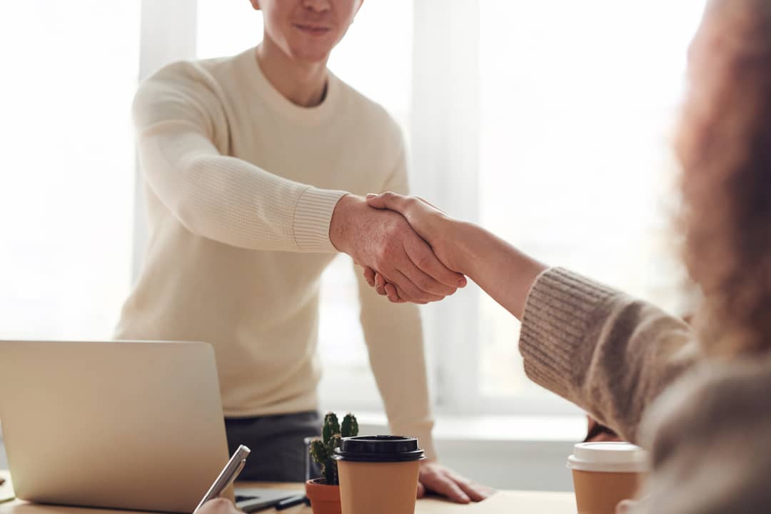 Illustrative image of two people shaking hands in an office setting.