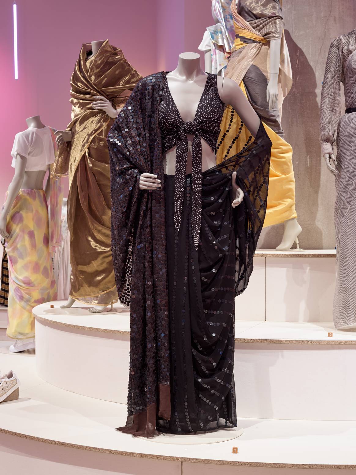 Schwarzer Sari mit geknoteter Bluse im Vordergrund; kombiniert mit weißem Crop-Top und Turnschuhen (links). Bild: Andy Stagg / Design Museum