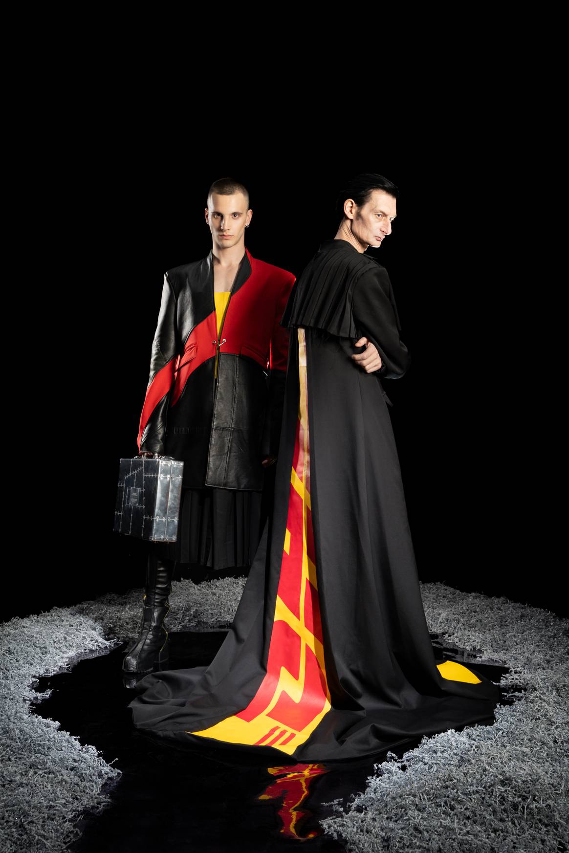 Lederblazer und Mantel mit Schleppe sind in den typischen Farben Schwarz, Rot und Gelb gehalten.